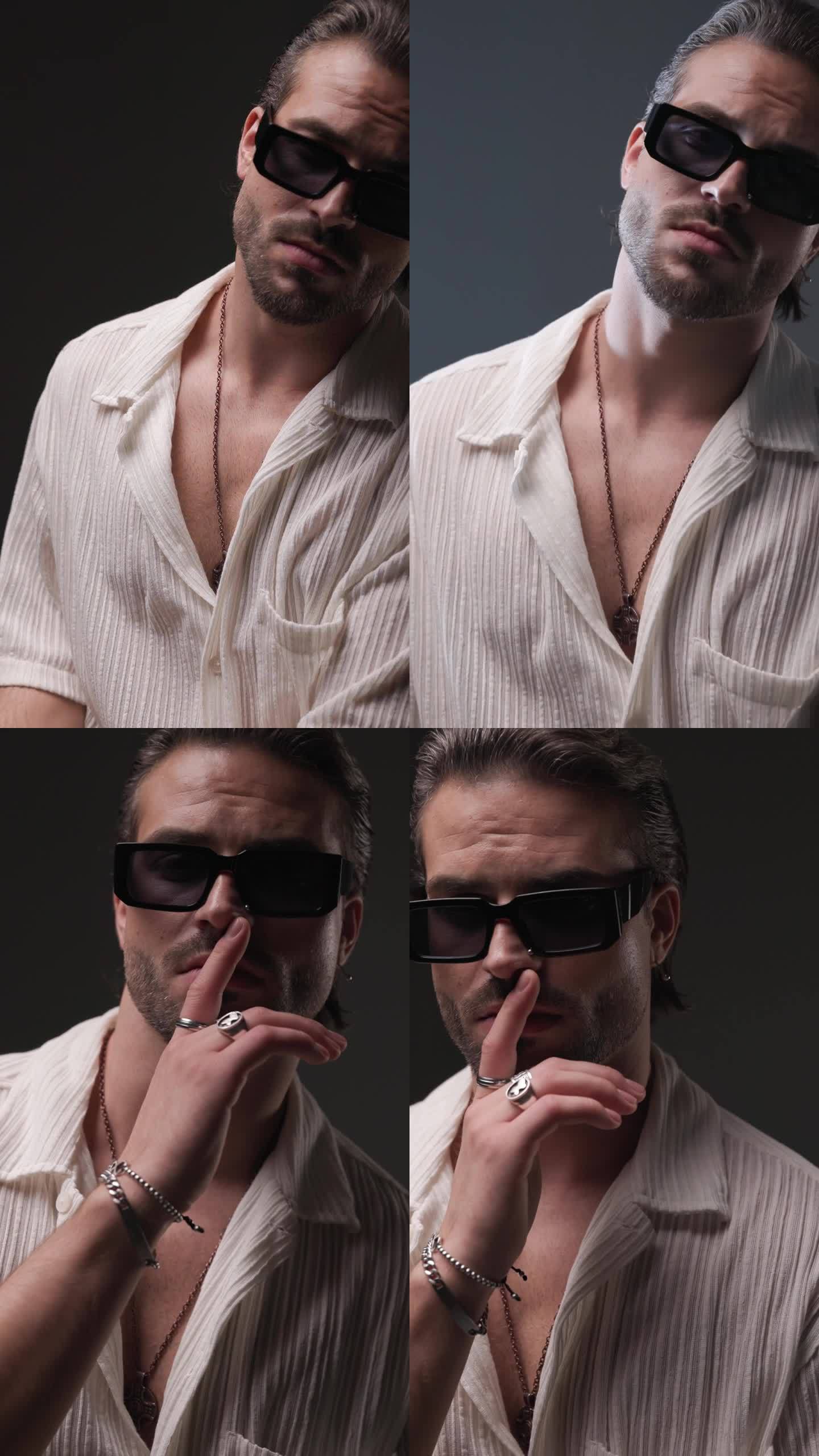 带着墨镜的性感休闲男人用手指触摸嘴唇，在闪光灯前做沉默的手势，灰色的背景