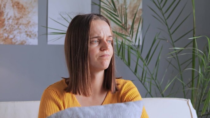 深感焦虑不安的年轻女子坐在家里的沙发上，感到孤独和悲伤，抱着枕头或与男友有一些分歧，表达抑郁