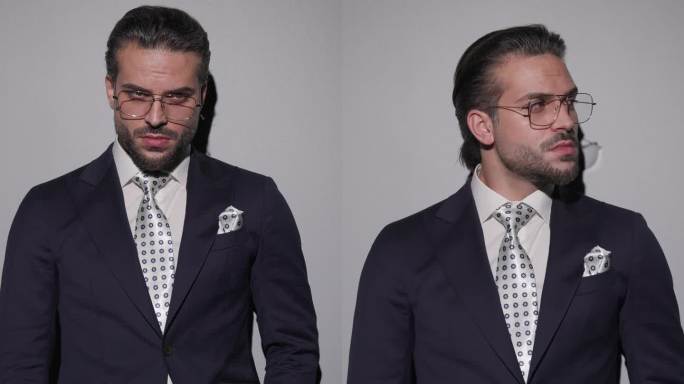 严肃优雅的男人，戴着眼镜，手插在口袋里，看向一边，在灰色的背景前整理西装