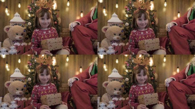 小女孩在大圣诞树前从圣诞老人那里收到她的圣诞礼物
