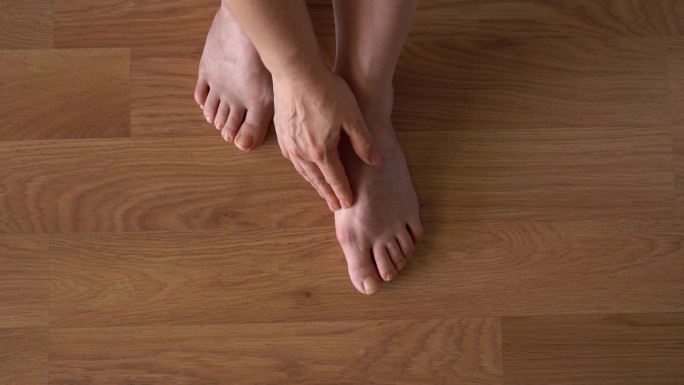 强化地板背景上女性腿上的拇外翻。一个女人腿上的肿块特写。从上面看。