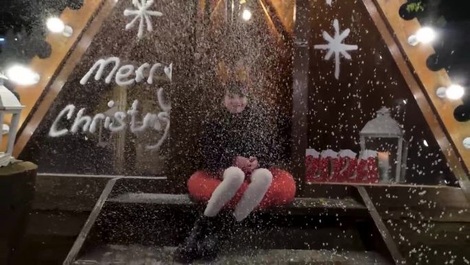 一个小女孩坐在山墙木屋前，开心地看着雪花飘落