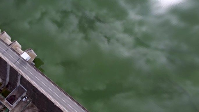 无人机拍摄的一条公路在大坝墙上的视频，水库里装满了水，倒映着云