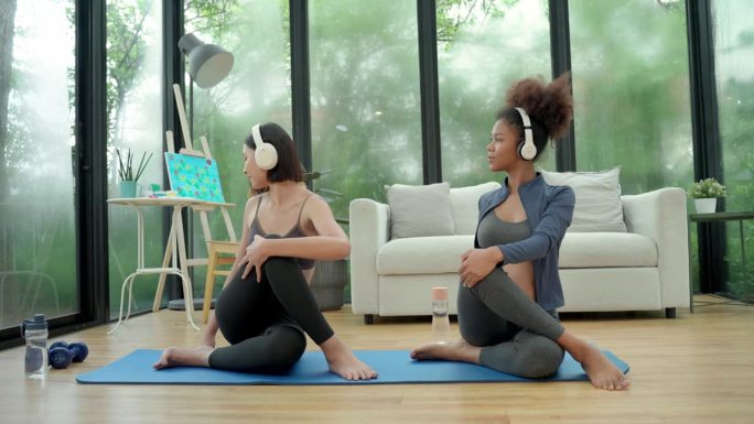 年轻的非洲孕妇和亚洲朋友一边听着平静的音乐，一边伸展身体，做瑜伽运动，以达到健康的生活方式和改善心理
