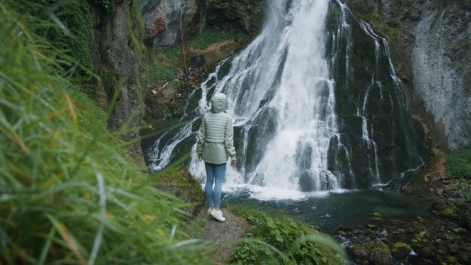 在奥地利高地欣赏格林格瀑布的女游客。女孩在森林里凝视着大自然的美