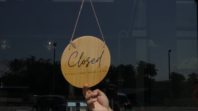男店主透过门玻璃打开招牌，准备服务。一个小企业主正在转动重新开放的标志。