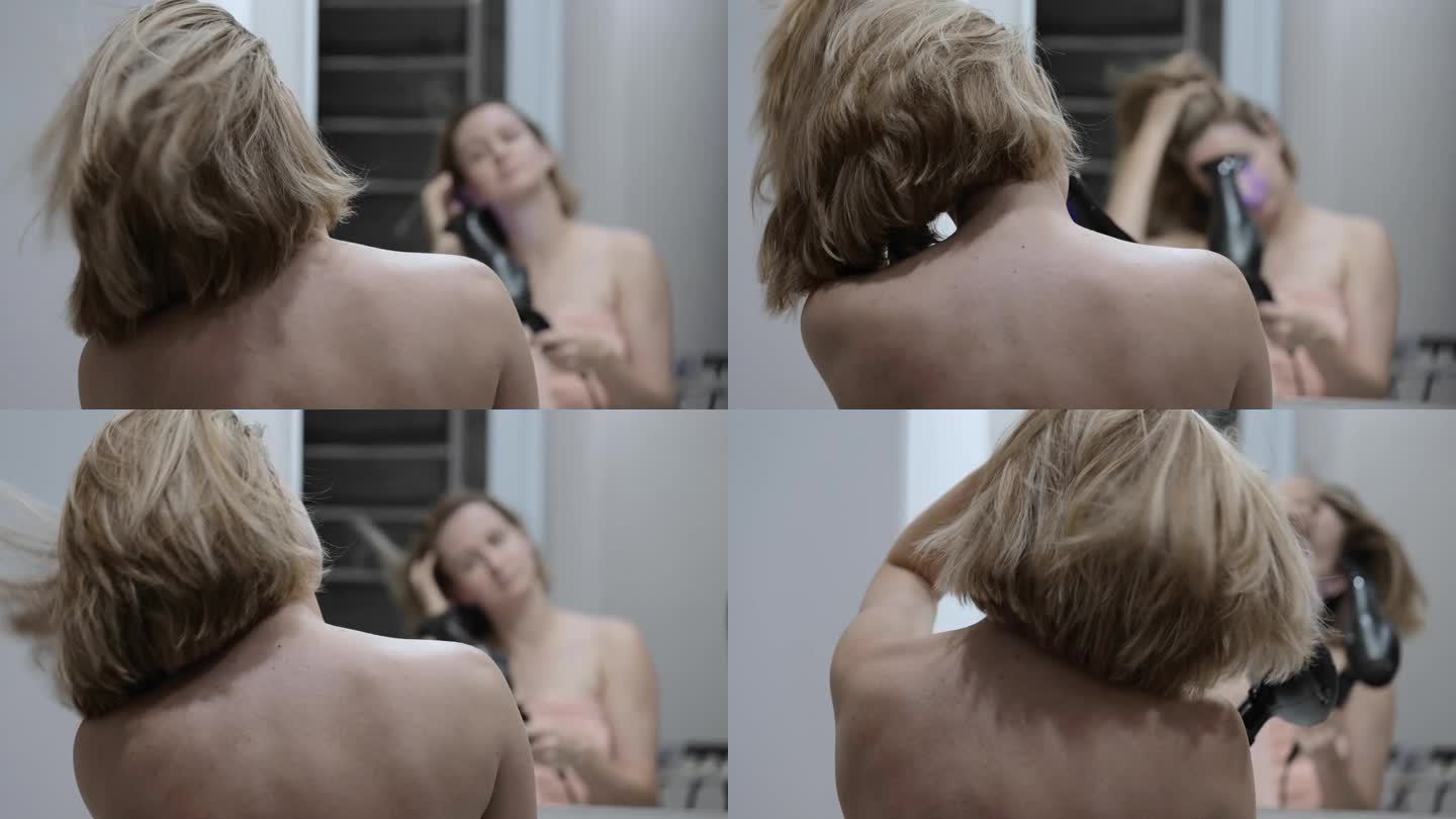 一位妇女用吹风机吹干头发。早上洗完澡后，一个女人在家里的浴室里做头发，吹干头发。一位年轻女子用电吹风