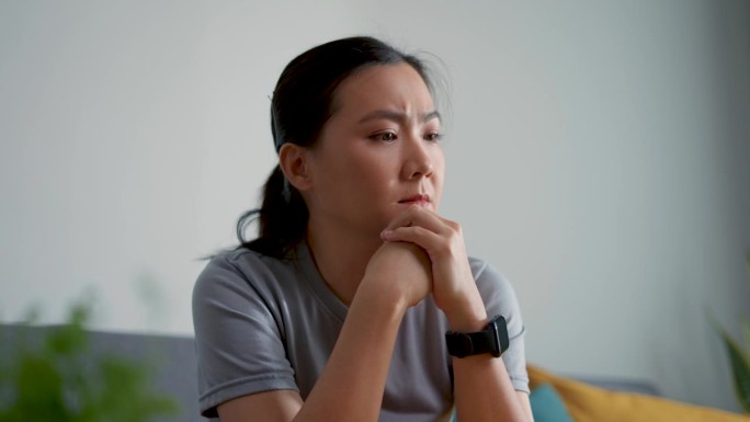 亚洲女人坐在沙发上思考问题，感到担忧和困惑。