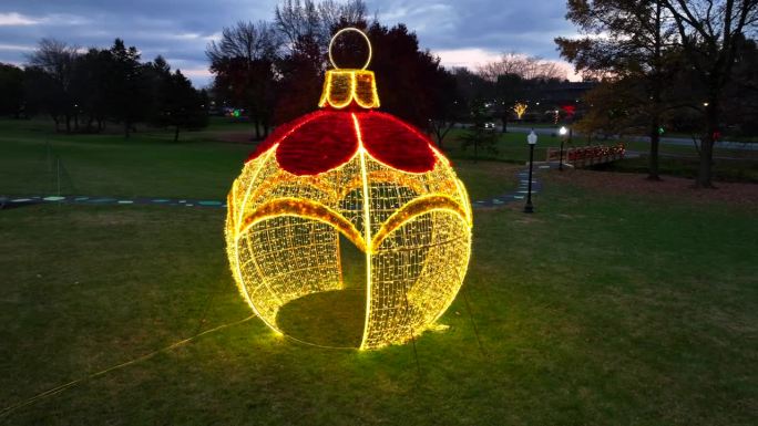 12月黄昏时分，美国公园草地上的大型照明圣诞装饰品和灯泡的航拍轨道照片。