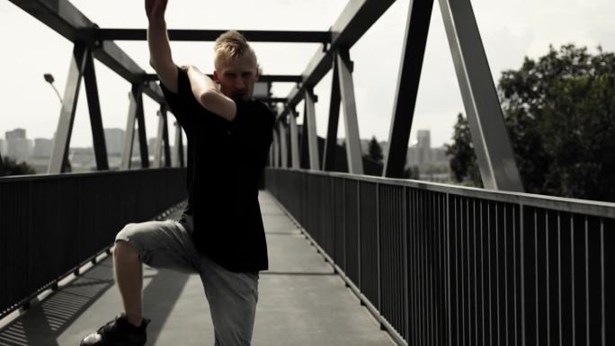 一名身穿黑色t恤的男子在吊桥上跳着动感十足的舞蹈。嘻哈在行动。金发美女舞者。