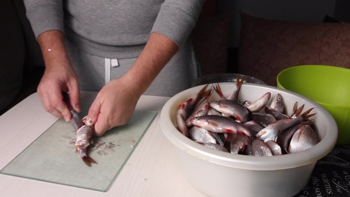 一个人会用刀把河里的鱼剖腹。在烤箱中烘干。他旁边是一个盛鱼的盆。