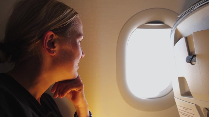 女乘客正在飞机上飞行。女孩坐在飞机上望着窗外去旅行度假旅行。旅行中的女性在飞机上享受飞行。旅行的女孩
