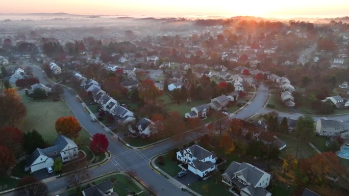美国的一个社区，秋天日出时雾气笼罩着两层住宅。空中展示的大郊区与色彩缤纷的秋叶。