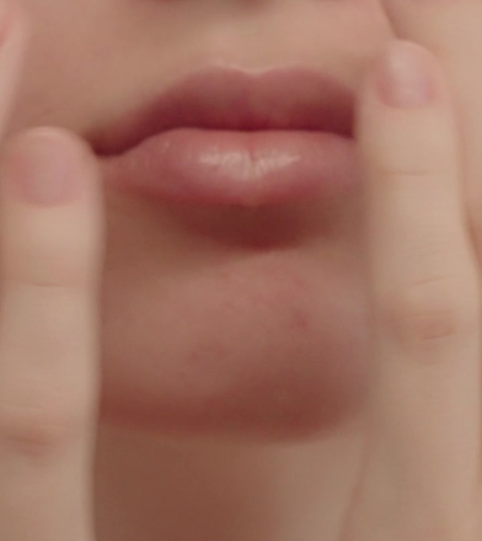 女性嘴唇和下巴的特写。女人抚平脸颊上的皮肤。
