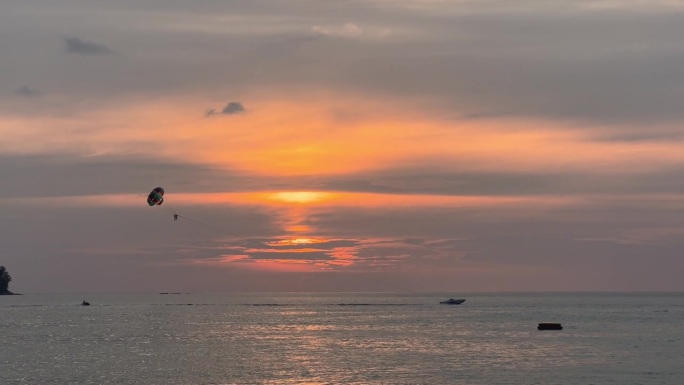 泰国海岸上的夕阳，沙滩上的娱乐活动——摩托艇后面的降落伞，人们在海面上跳伞