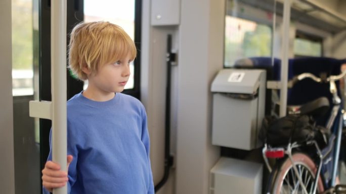 青春期前的男孩在地铁车厢或火车上旅行。一个孩子看着火车窗外的风景。一辆通勤火车开动时，一名年轻乘客紧