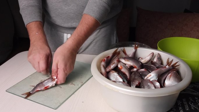 一个男人用刀清洗河里的鱼。在烤箱中烘干。他旁边是一个盛鱼的盆