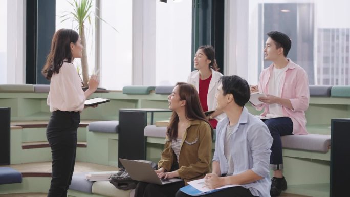 在办公室的会议室里，中年亚洲女商人站在她的同事面前，展示她的商业战略想法，分享她提高商业利润的经验。