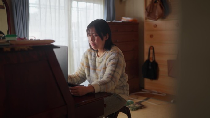 穿着休闲服的亚洲女性在家里使用笔记本电脑