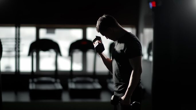 一个意志坚定的男人的剪影，穿着运动服，在健身房的室内避难所举重，将自己推向极限