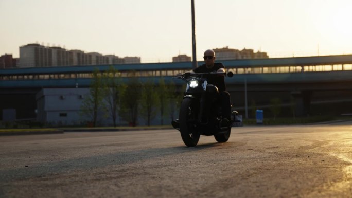 一个黑衣男子骑着自行车穿过停车场。摩托车在镜头中移动。一个骑自行车的人骑在被阳光照耀的柏油路上。地铁