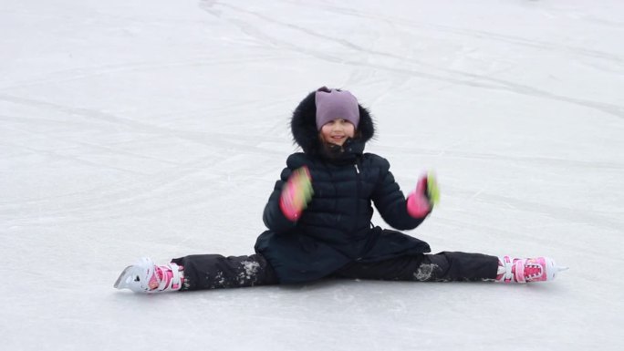 冬天的乐趣和娱乐。花样滑冰的小女孩在滑冰场做劈叉动作。
