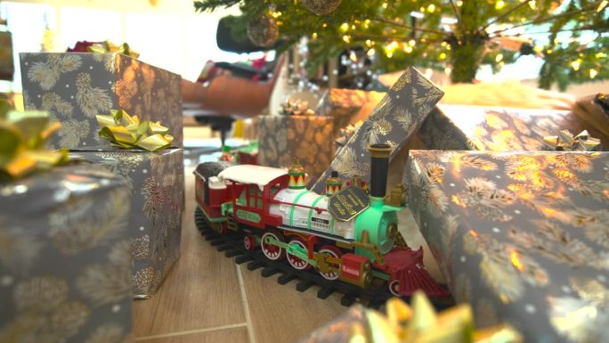 迷人的素材:在节日圣诞树下滑翔，礼物丰富，展示模型火车，在一个令人愉快的大范围反向滑动镜头中传播快乐