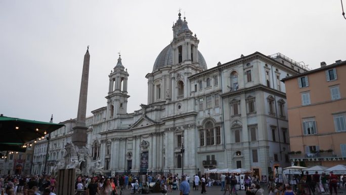 意大利罗马- 2023年9月3日。17世纪巴洛克式教堂的正面，面对纳沃纳广场，人们在阴天走来走去。