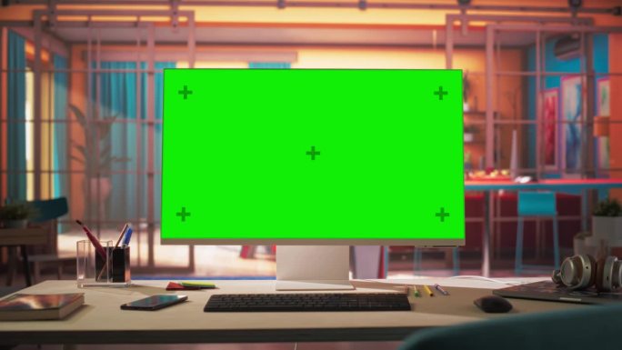 站在一个舒适的家庭办公室的桌子上，放大现代个人电脑显示器与色度键绿色屏幕显示。客厅由室内设计师设计，