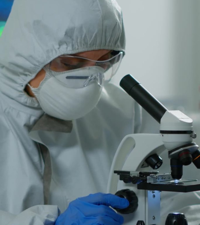 垂直视频:穿着防护服的女科学家在实验室使用现代显微镜工作