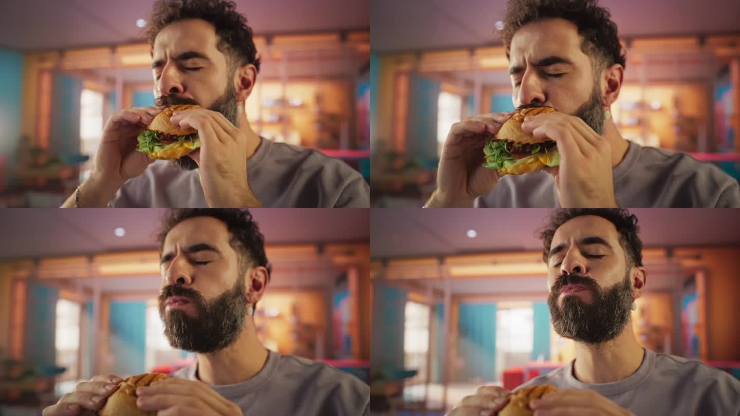 快餐品牌商业概念:一个留着胡子的年轻时尚男子的慢动作肖像，他看着镜头，微笑着咬一口美味的汉堡。纯粹享