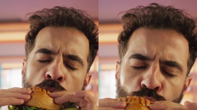 垂直屏幕:追踪一个正在家里享受美味汉堡的男人的慢动作肖像。一个快乐的男人点了快餐，五彩缤纷的环境，高