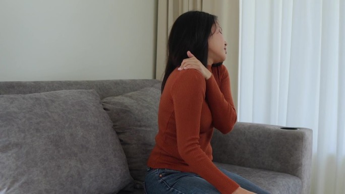 亚洲女少女因工作疼痛伴腰痛，抱着按摩揉肩痛或酸痛，在家坐在沙发上疼痛。医疗保健的人。