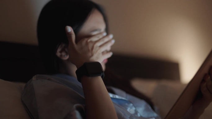 一名亚洲女性在晚上使用数码平板电脑时眼睛受到刺激