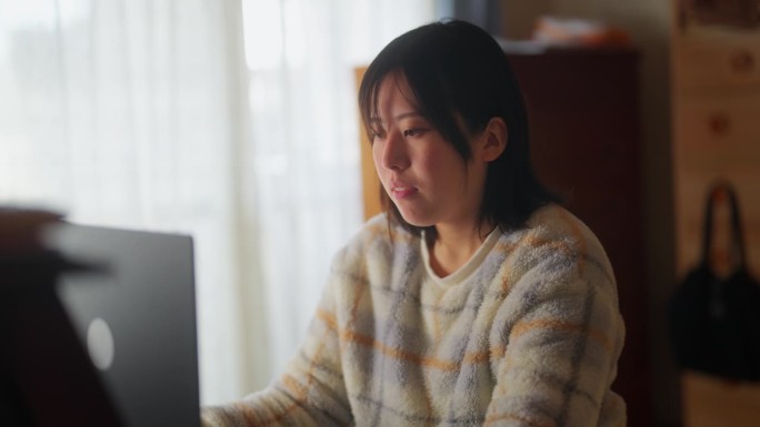 穿着休闲服的亚洲女性在家里使用笔记本电脑