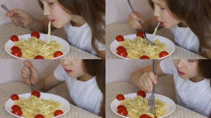 一个小女孩在厨房里吃意大利面。可爱的学龄前孩子在吃奶酪和西红柿面条。意大利面螺旋