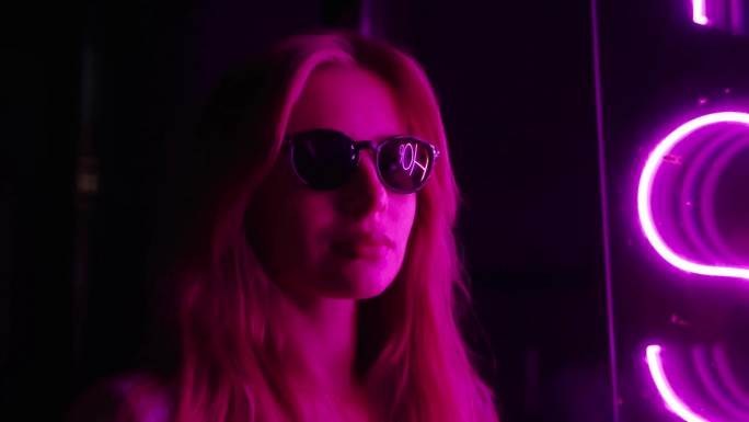 一个戴着墨镜的漂亮女孩的眼镜反射出粉红色的霓虹。一个女孩在夜晚的肖像。