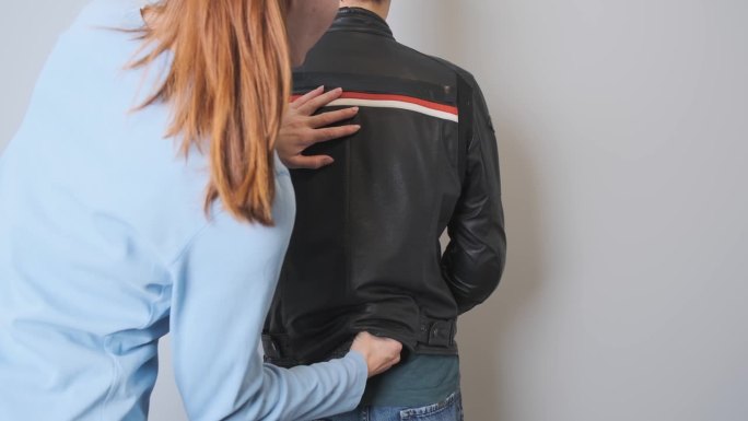 一个女人从一个男人穿的摩托车夹克里拿出一个护背器。将塑料贴在背面，从背面看。塑料盾牌的演示。