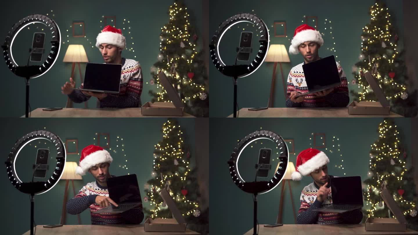 男博主在圣诞节在家拆笔记本电脑的同时，用现代智能手机录制视频内容。阿拉伯影响者对现代小工具进行评论