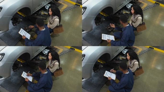 黑人机械师在检查了车辆并在剪贴板上做了记录后，向女顾客解释了汽车悬挂系统的坏消息