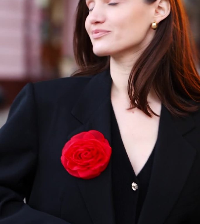 一个美女的特写，穿着黑色夹克，胸前插着一朵红花，看着镜头摆姿势。垂直视频。商业女士。