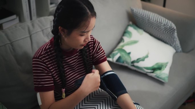 一名携带血糖传感器的亚洲少女正在家中使用数字血压仪