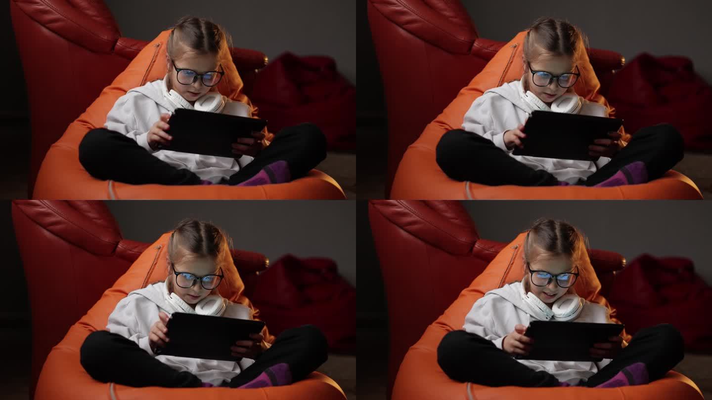 兴奋的少女坐在家里的沙发上，用数字平板电脑技术设备玩游戏。情绪化的孩子戴着眼镜拿着pad电脑上网。儿
