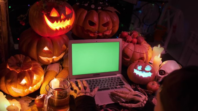 骷髅手，打开笔记本电脑，绿屏闪烁着雕刻的南瓜，旁边是啤酒杯的节日背景