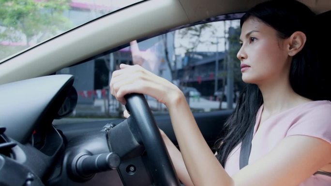 亚洲女司机穿着休闲装坐在车里，在城市开车时看起来很直。快乐的女商人透过窗户看着马路，开车在城市里转悠