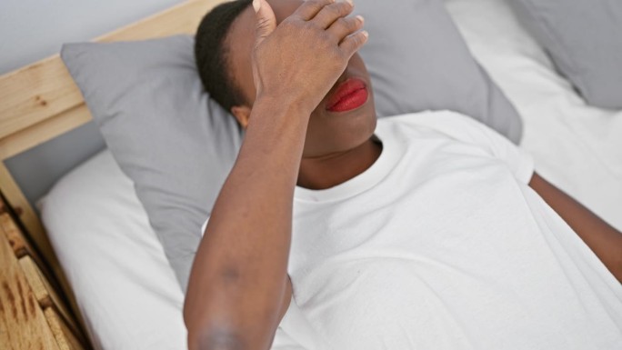 悲伤的非裔美国女人用手蒙住眼睛，躺在卧室的床上，失明，躲藏，拒绝的概念