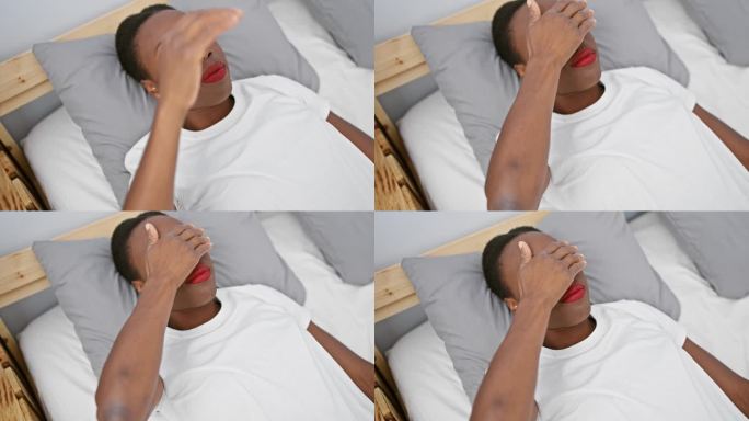 悲伤的非裔美国女人用手蒙住眼睛，躺在卧室的床上，失明，躲藏，拒绝的概念