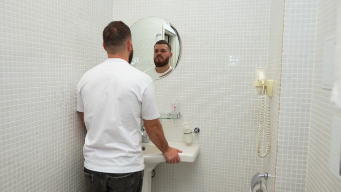 年轻英俊的大胡子男子对着浴室镜子里的自己说话