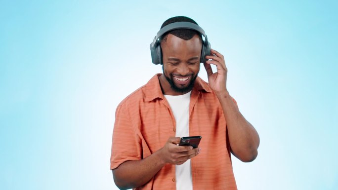 黑人，带着智能手机和耳机跟着音乐跳舞，在演播室里听蓝色背景的广播。舞蹈，乐趣和能量与锐舞或技术，音频