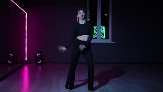 住相机。专业舞蹈女子在霓虹灯的黑暗大厅里。在做动作时主动摆动手臂和做手势。